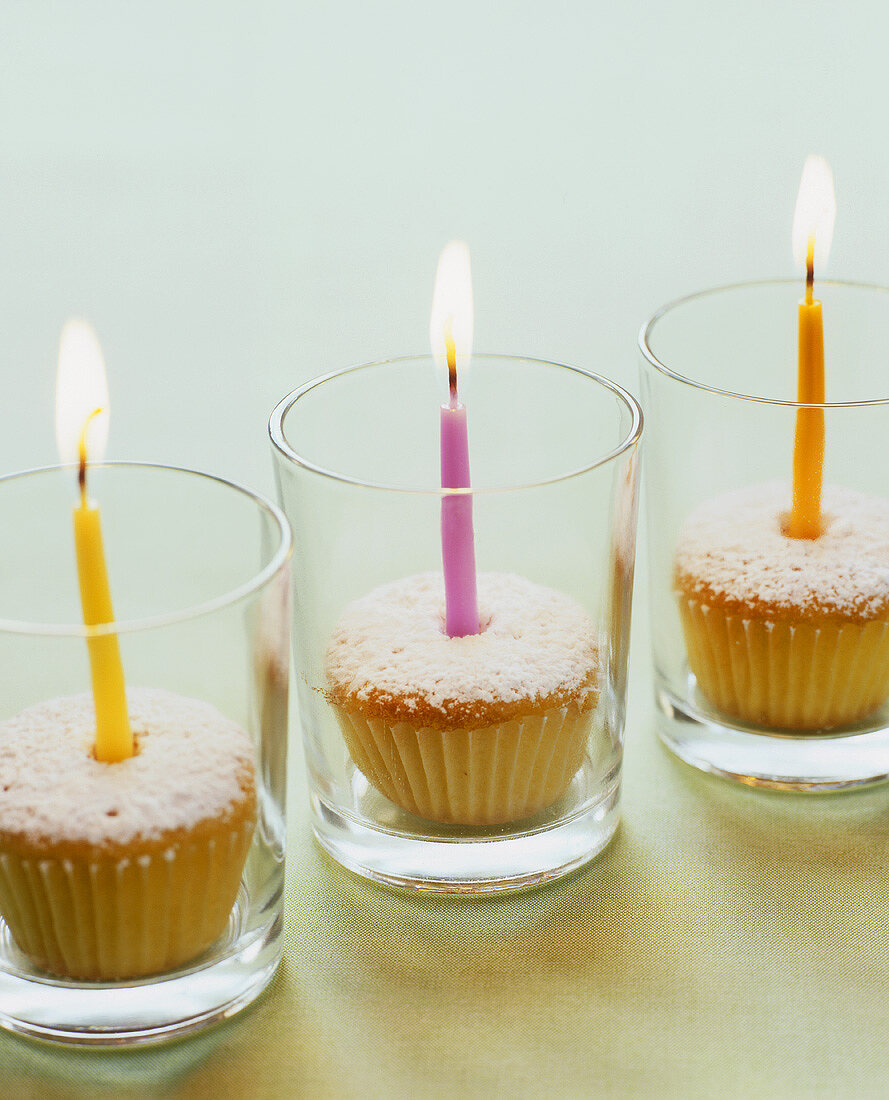 Three cupcakes with burning candles in glasses