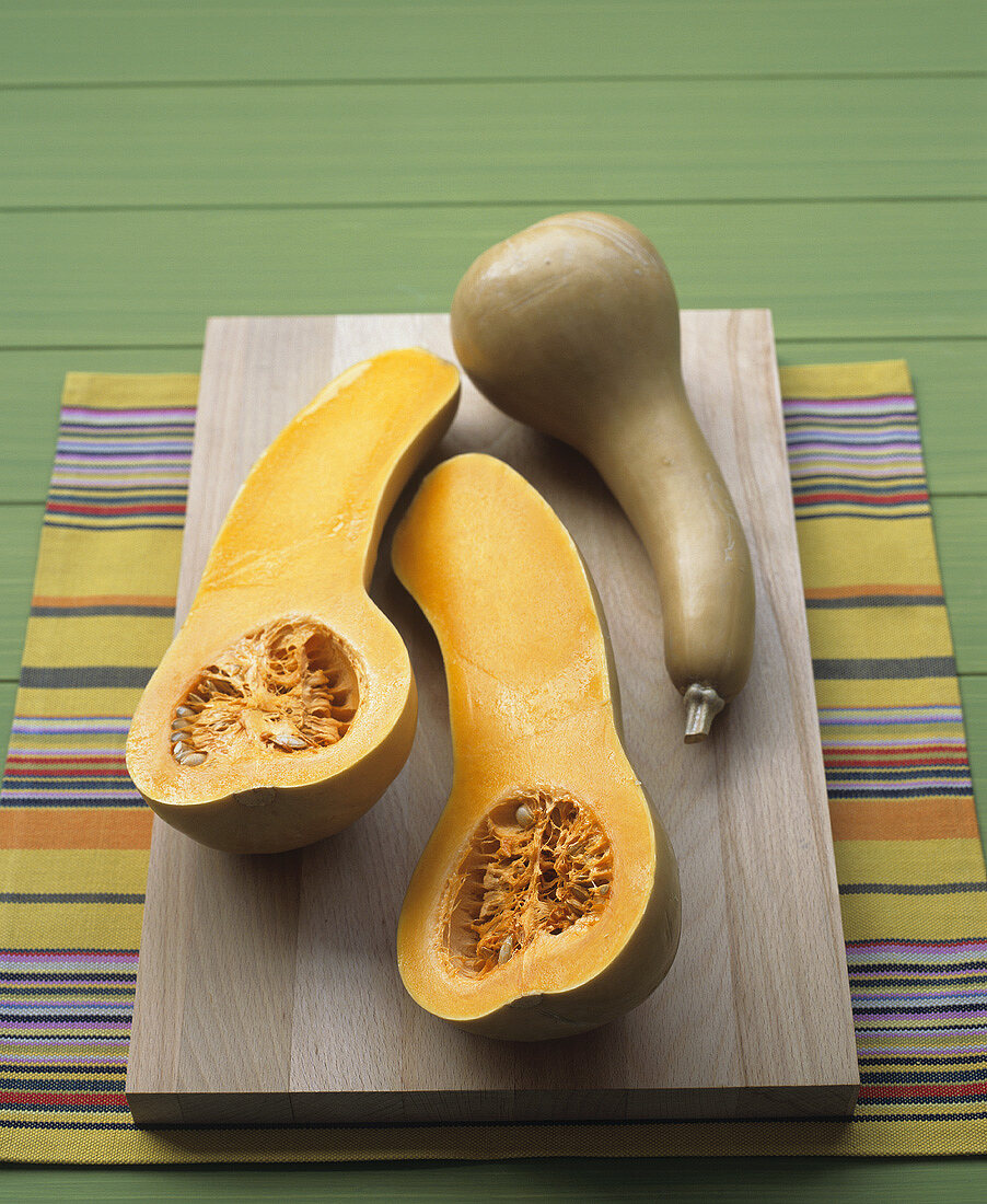 Whole and halved butternut squashes on a wooden board