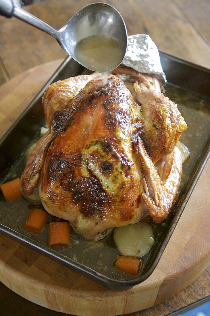 Turkey in a roasting tin being basted with roasting juices