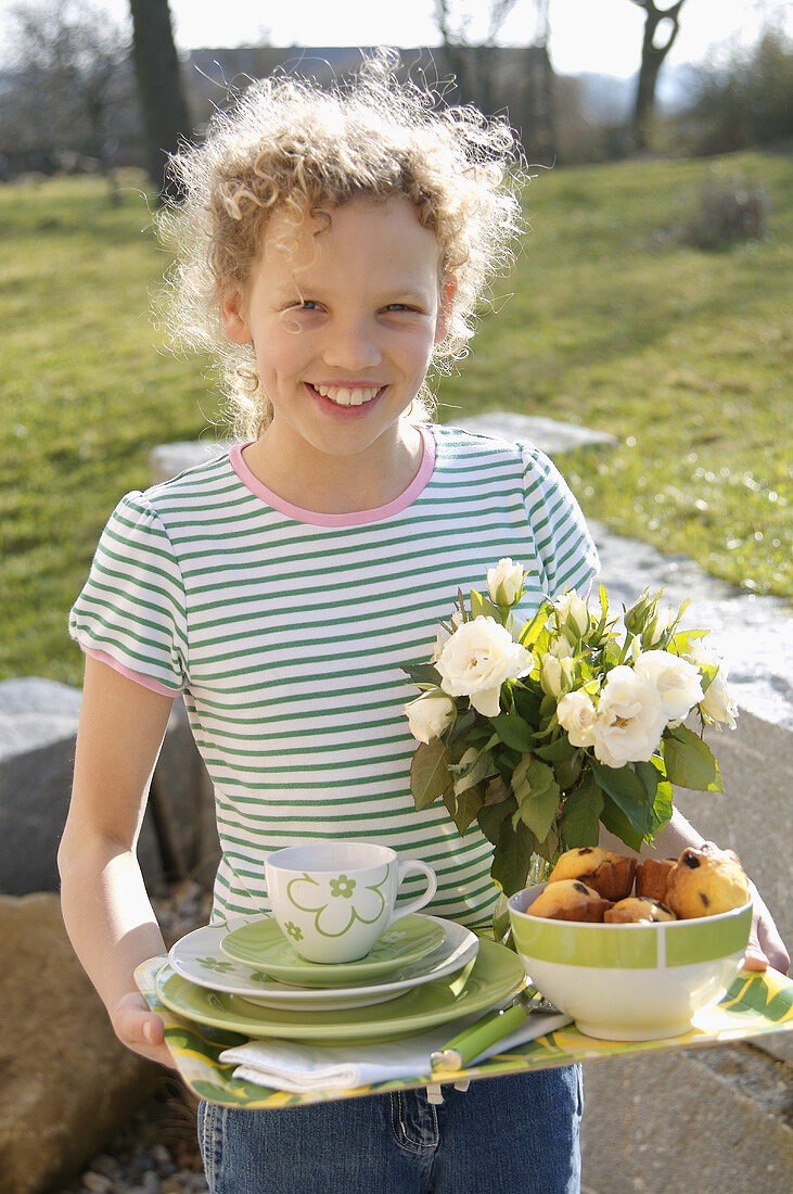 Curly-haired girl carrying tray for breakfast out of doors