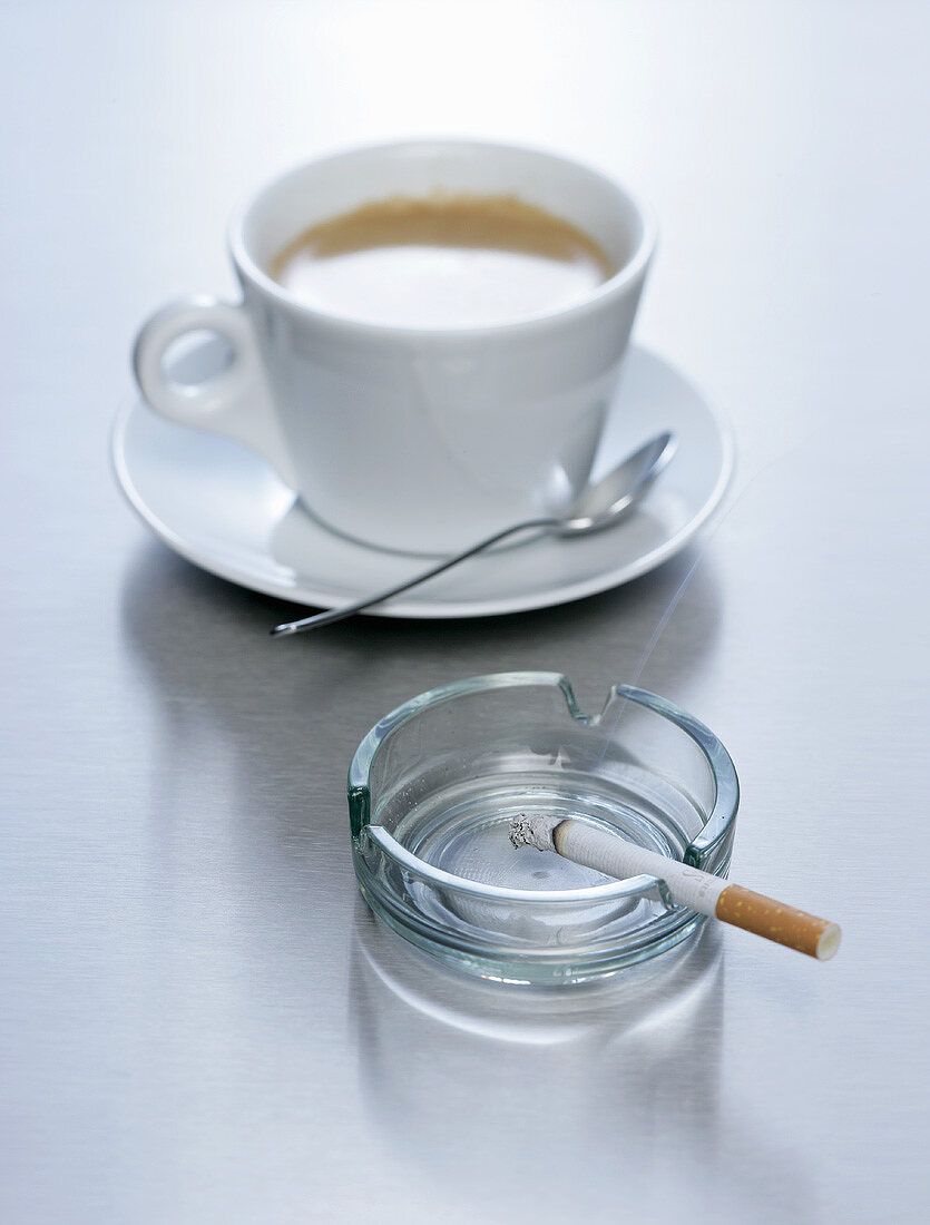 A cup of coffee with a cigarette in an ashtray