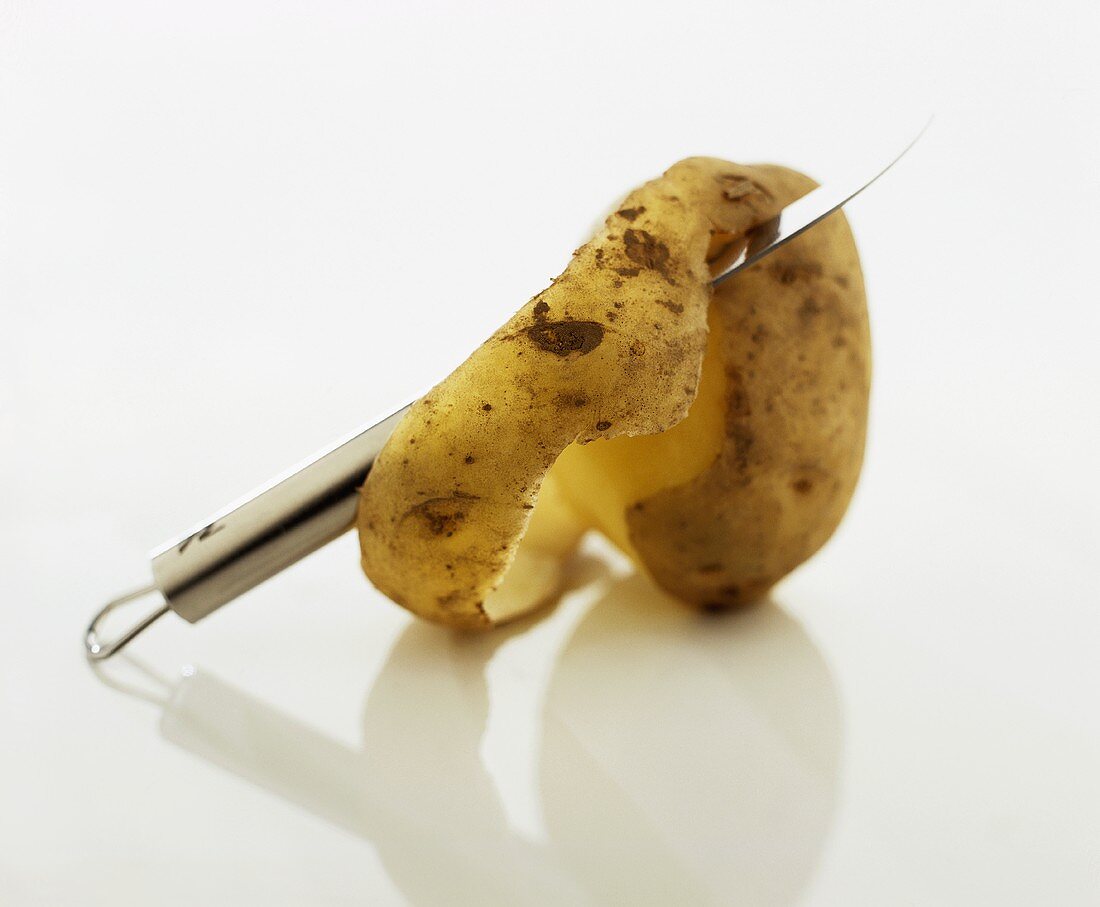 A raw, half-peeled potato with a knife