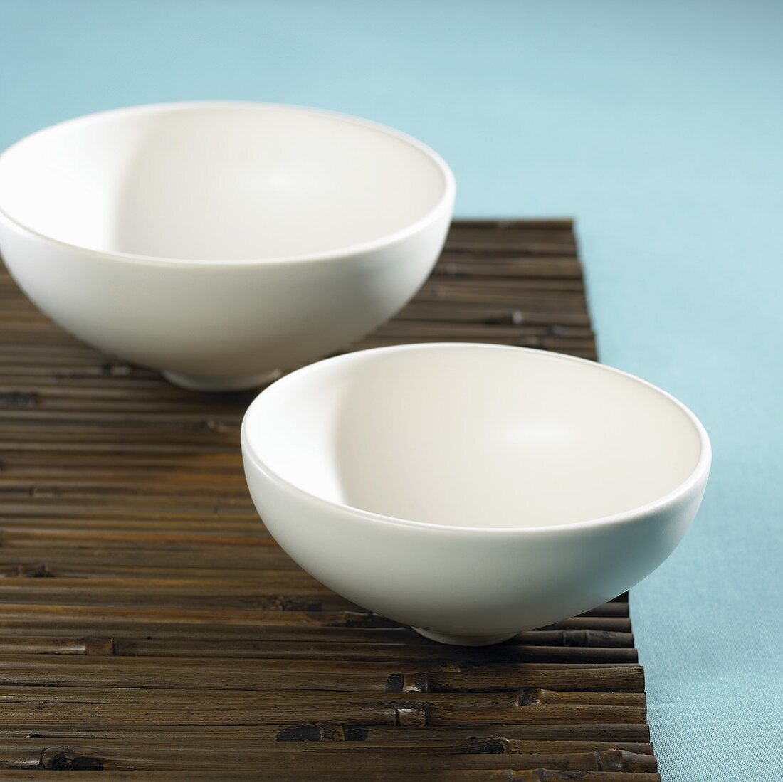 Two porcelain bowls on a bamboo mat