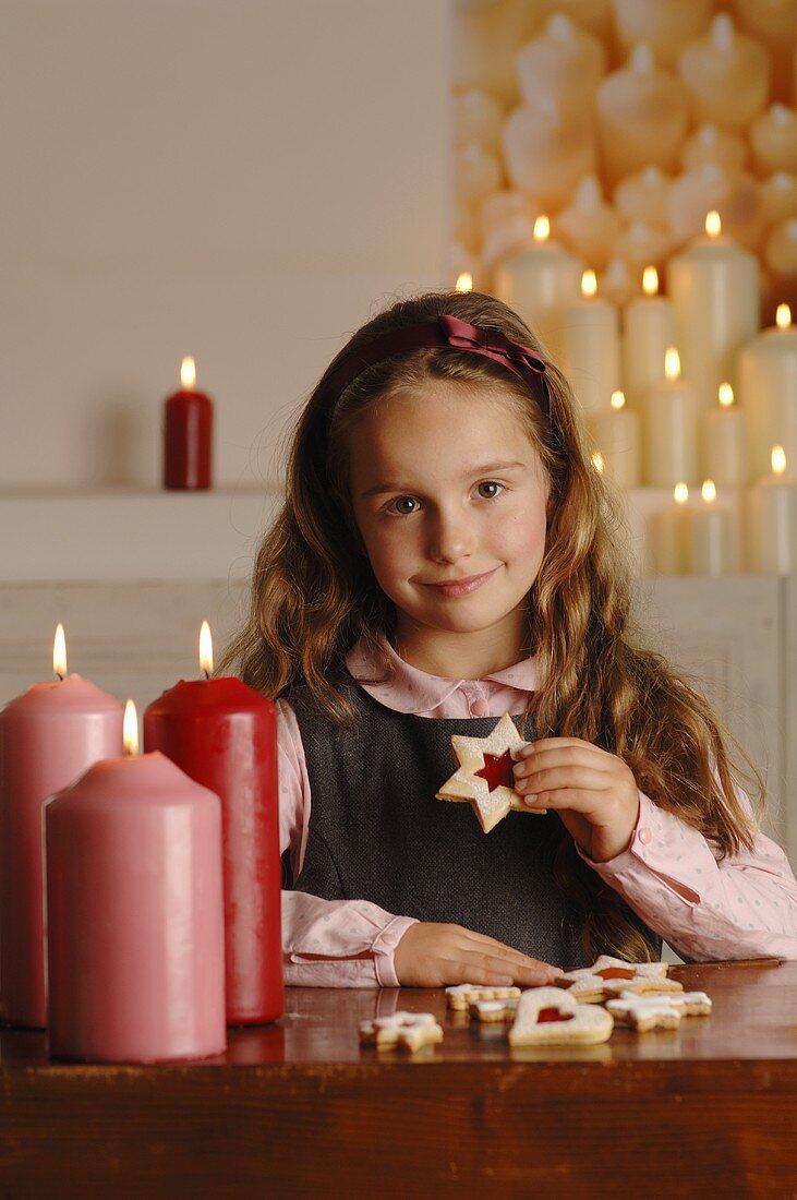 Mädchen sitzt am Tisch mit Kerzen und Weihnachtsplätzchen