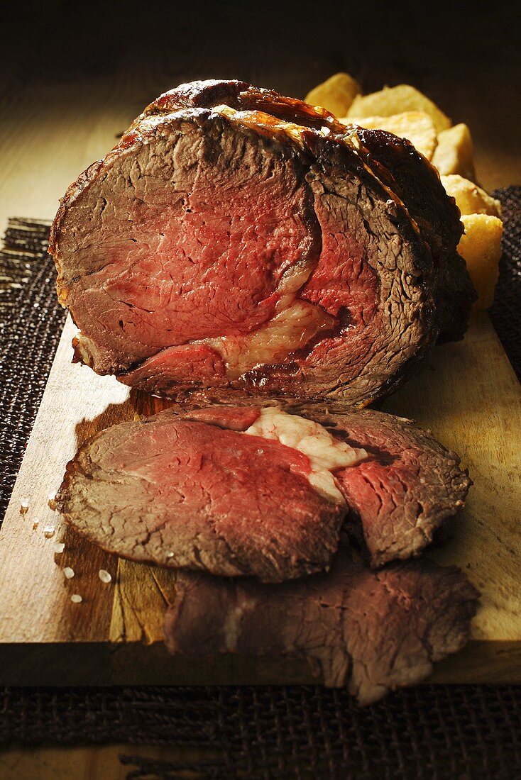 Roast beef, partly carved, & roast potatoes on wooden board