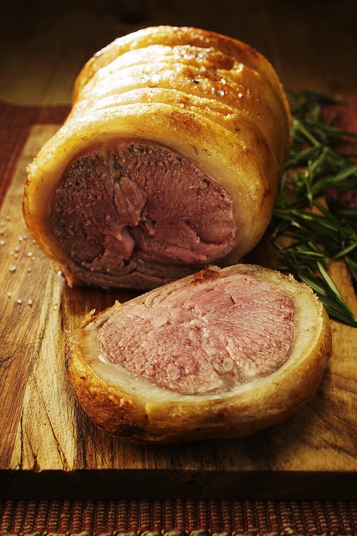 Roast saddle of lamb, partly carved, with rosemary on board
