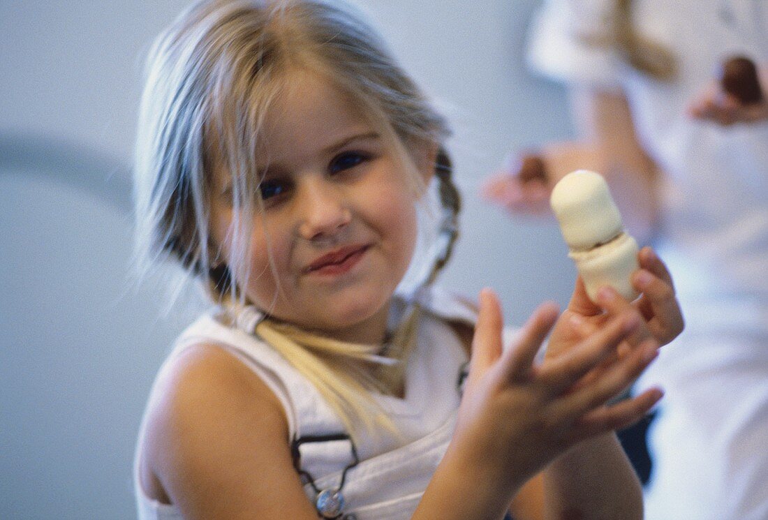 Little girl with two chocolate-coated marshmallows in her hand