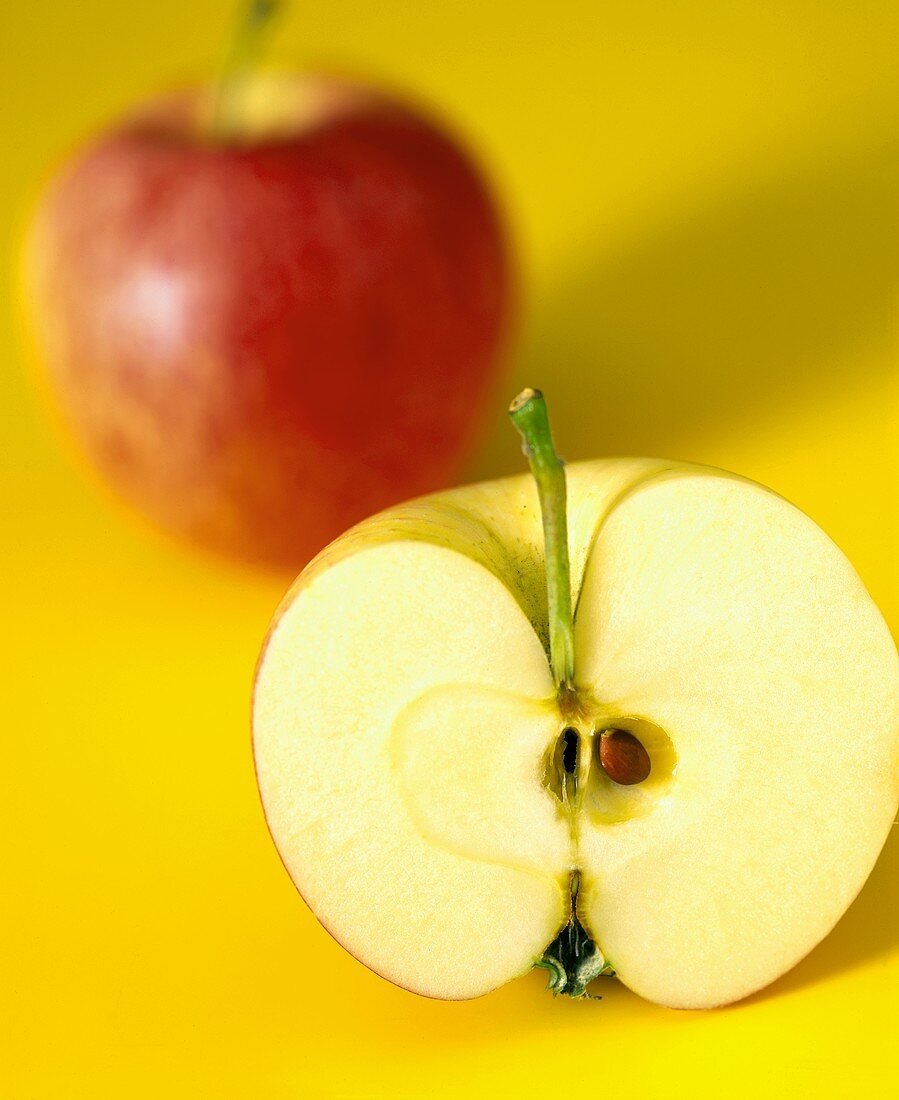 Ein ganzer Apfel und eine Apfelhälfte auf gelbem Untergrund