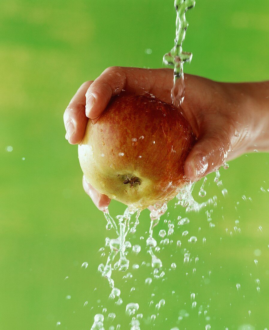 Hand hält Apfel unter Wasserstrahl, grüner Hintergrund
