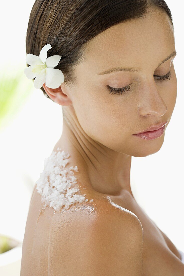 Portrait of young woman with a flower in her hair and exfoliating scrub on her back