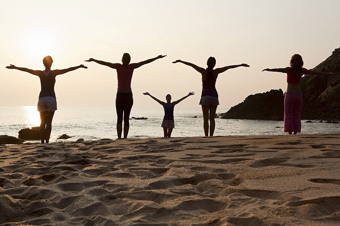 Frauen praktizieren Yoga am Strand bei Sonnenuntergang