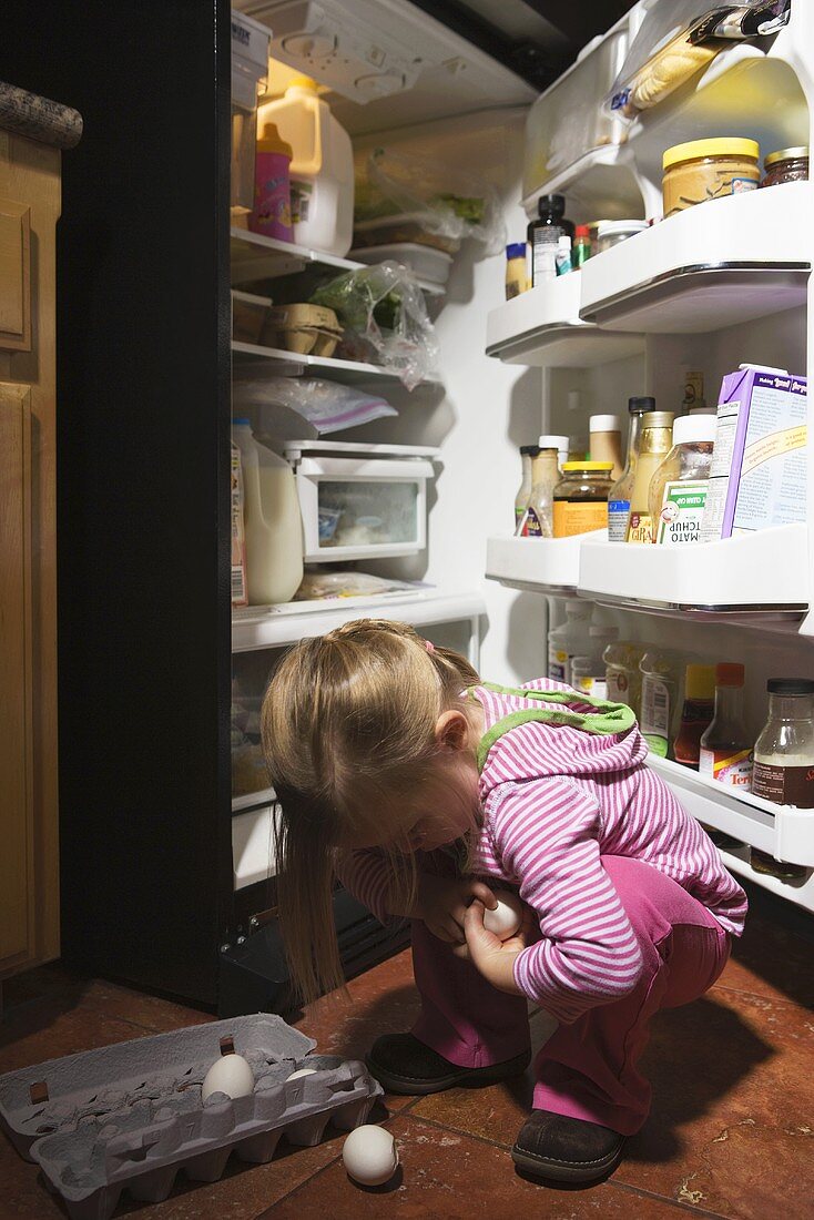 A girl in front of a fridge picking up dropped eggs