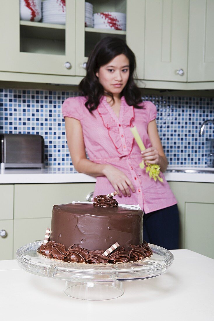 Junge Frau isst Sellerie mit Blick auf Schokoladenkuchen