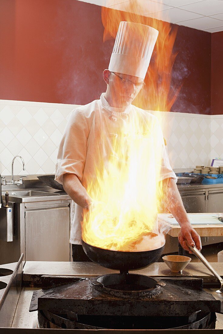 A chef cooking in a commercial kitchen, partially hidden behind a flame