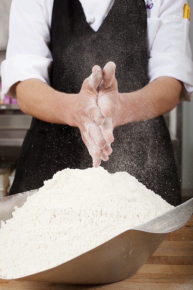A chef rubbing flour on his hands in a commercial kitchen