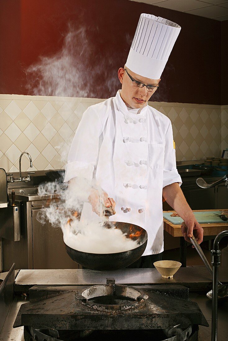 Koch brät mit Wok in einer gewerblichen Küche