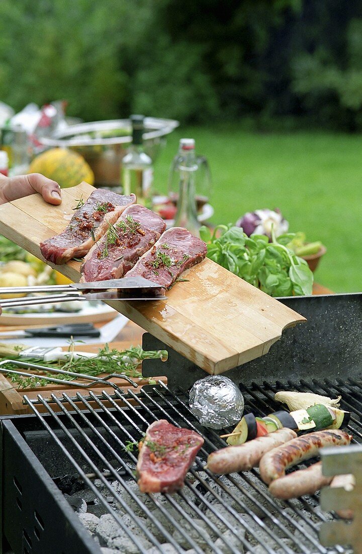 Steaks being placed on a barbeque.