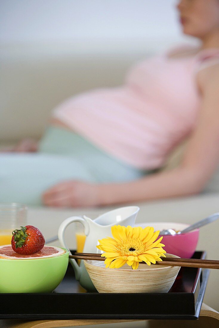 Schalen von Früchten auf einem Tablett, dahinter schwangere Frau