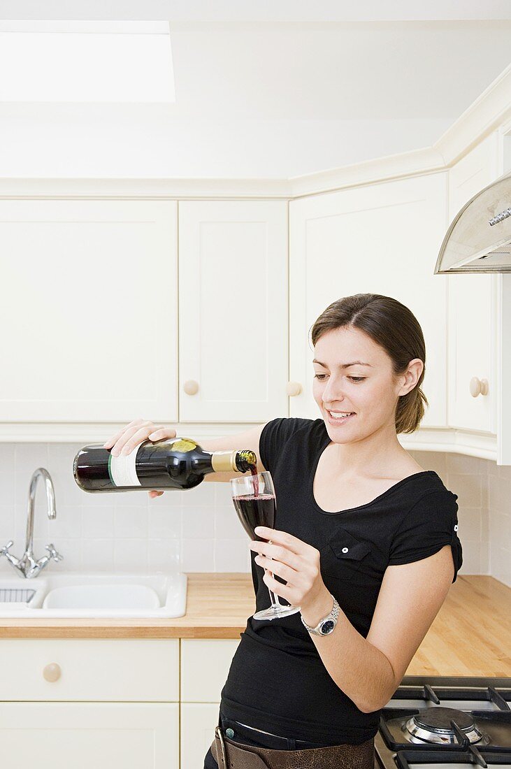 Frau giesst sich Glas Rotwein ein