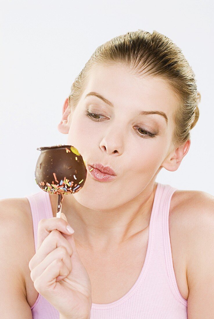 A young woman eating a chocolate-coated apple