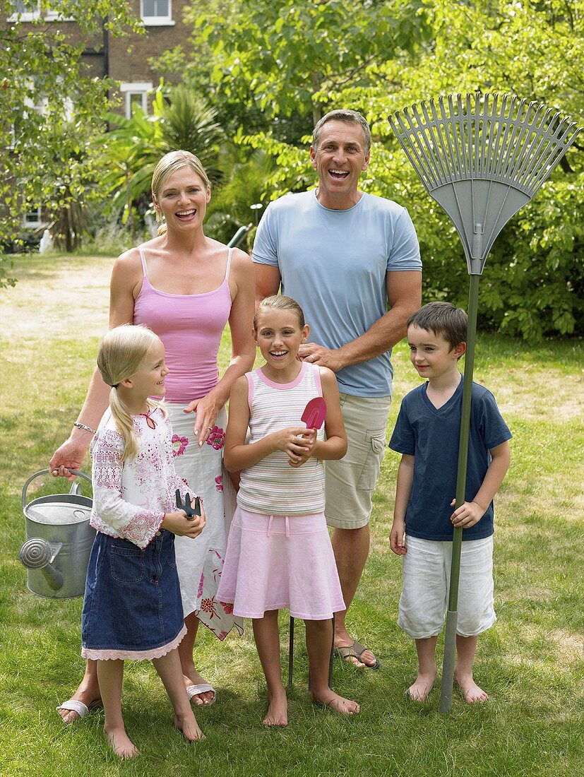 Familie steht mit Gartenwerkzeugen im Garten