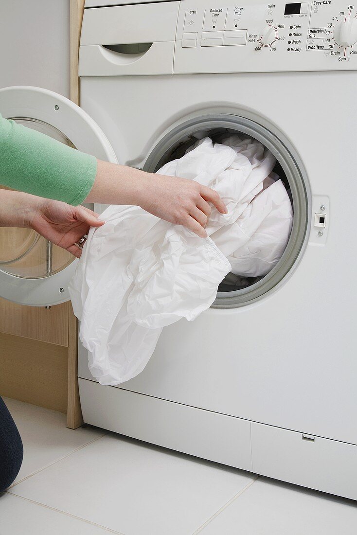A woman taking a sheet out of a washing machine