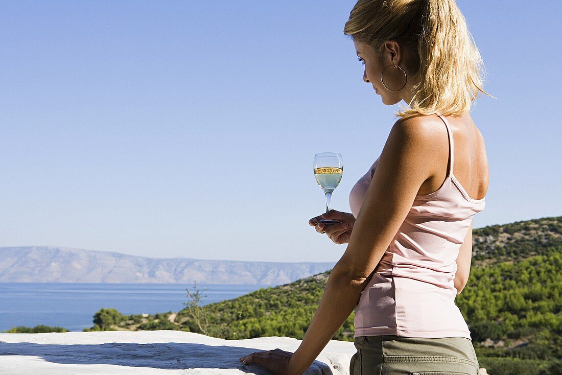 Frau hält ein Glas Weißwein mit Ausblick auf einen See