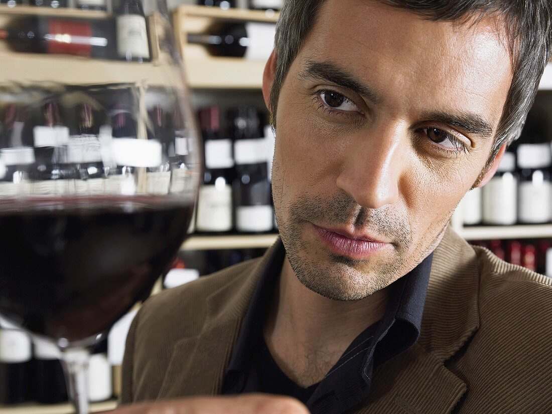 A man looking at a glass of red wine