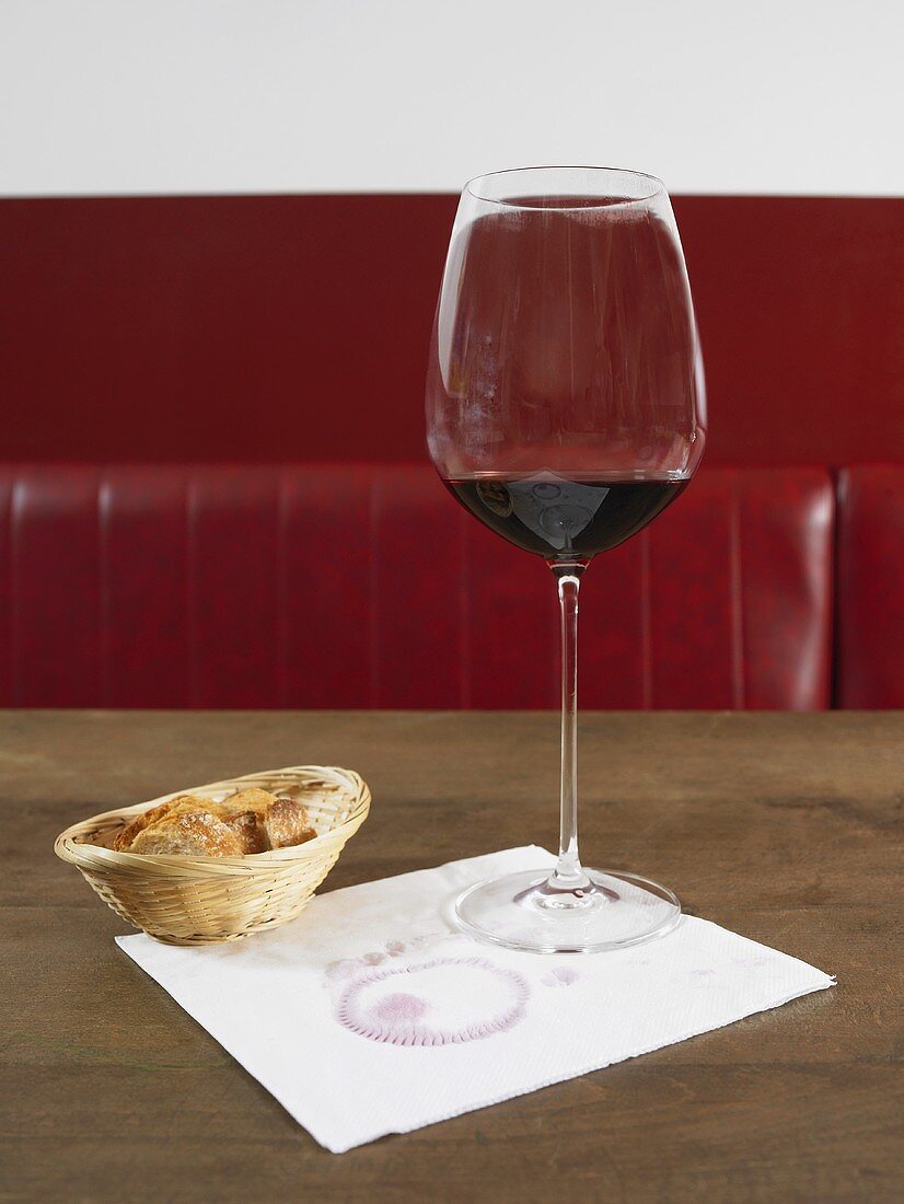 A glass of red wine on a napkin with a bread basket