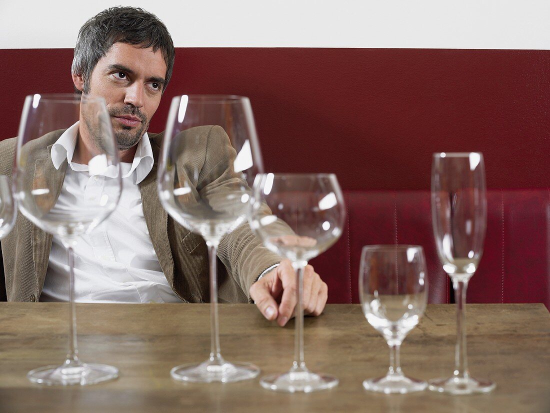 Mann sitzt mit verschiedenen leeren Weingläsern am Tisch