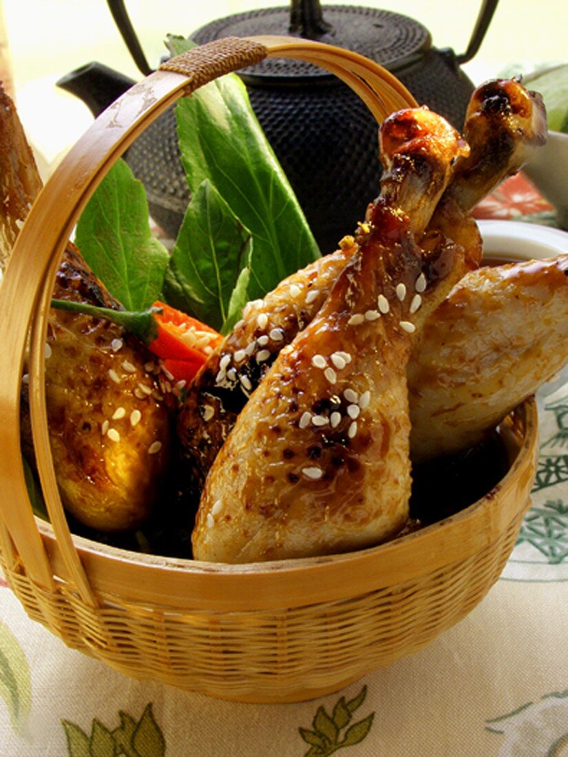 Asiatische Hähnchenkeulen mit Sesam im Korb; Teekanne