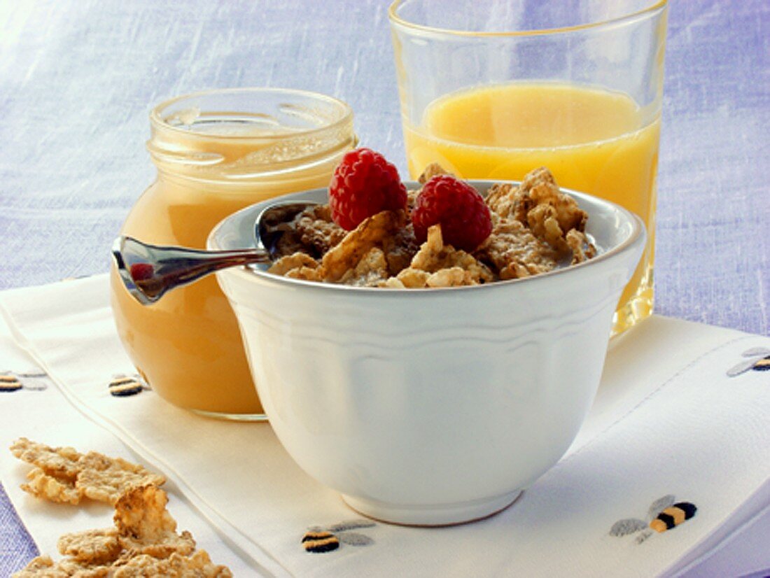 Vollkorn-Cornflakes mit Himbeeren; Honigglas; Orangensaft