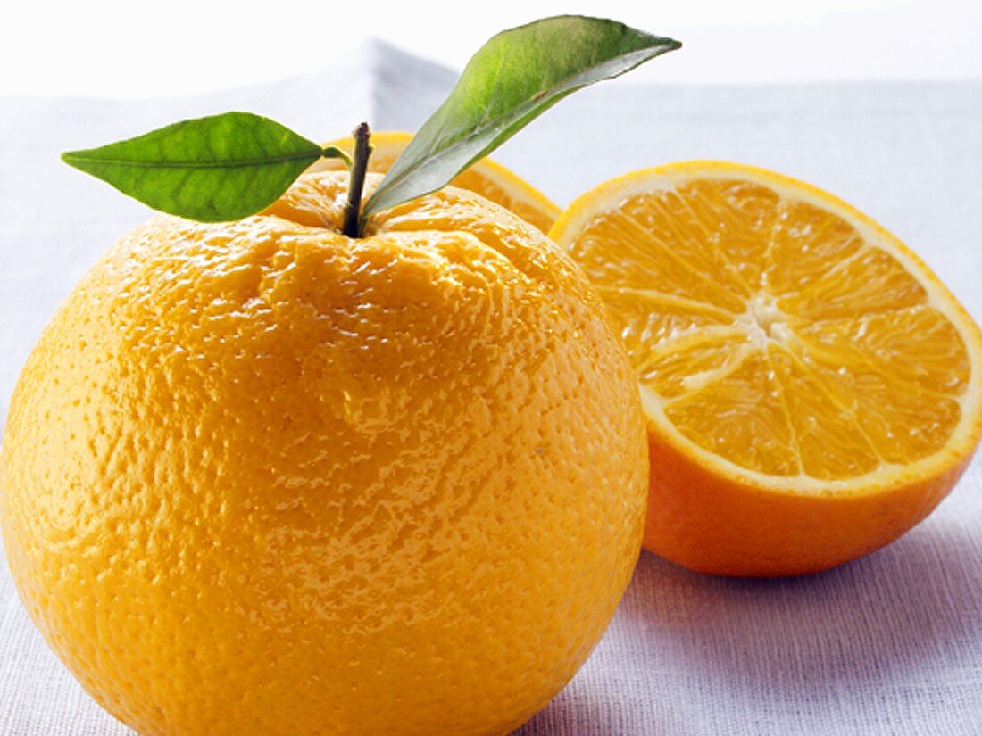 Orange mit Stiel und Blättern und Orangenhälfte