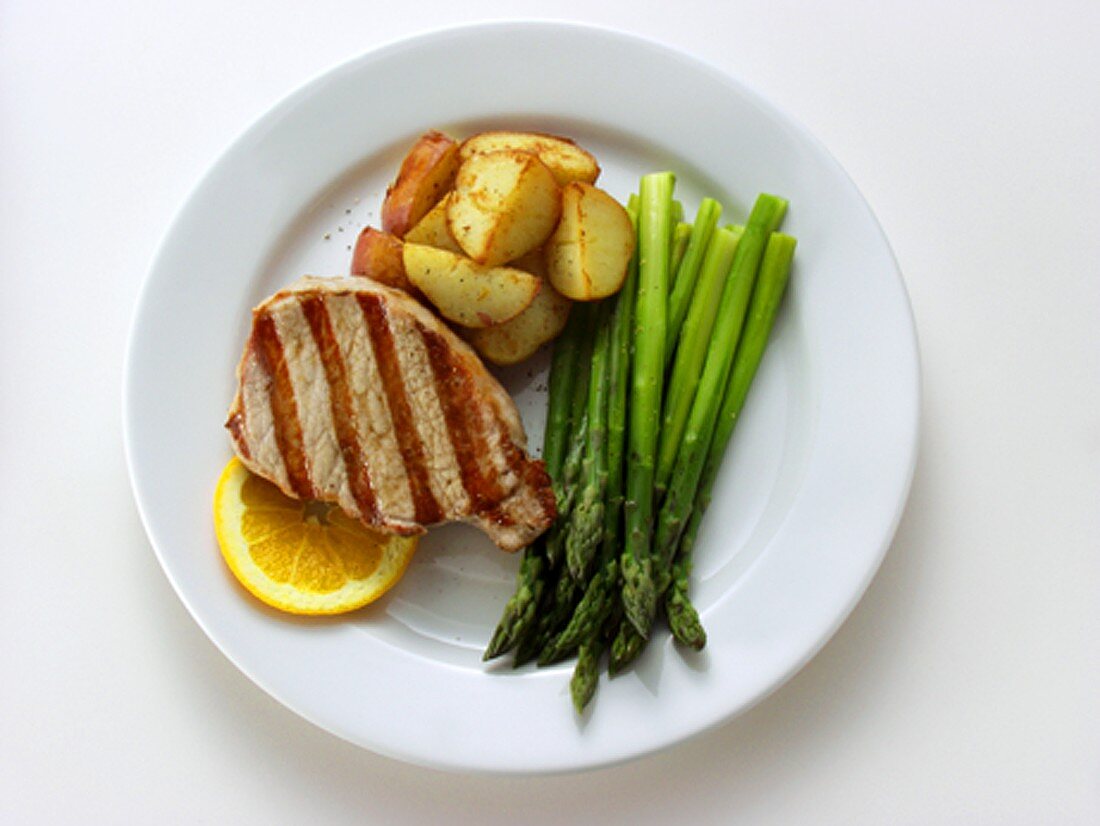 Pork steak with green asparagus, fried potatoes, orange