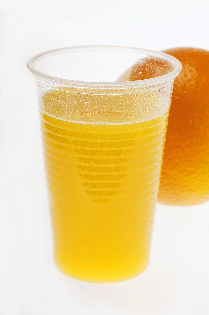 Orange juice in plastic tumbler in front of orange