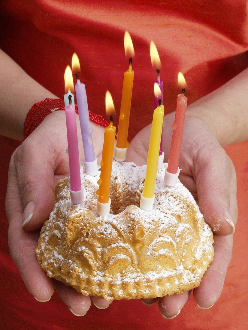 Hände halten kleinen Napfkuchen mit brennenden Kerzen