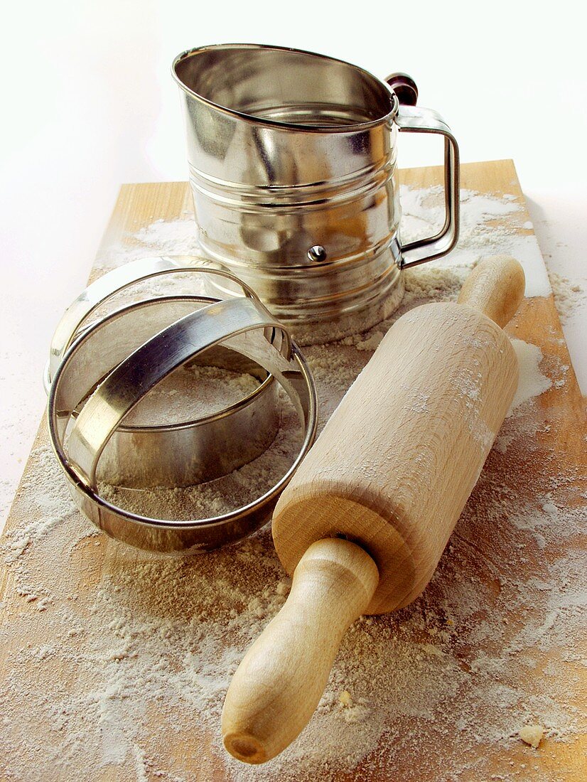 Rolling pin, cutters and flour sieve on wooden chopping board