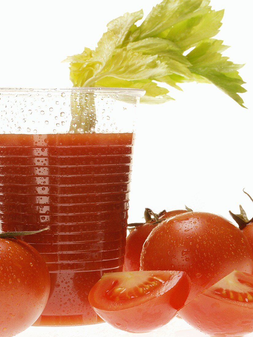 Tomato juice in plastic tumbler with celery; tomatoes