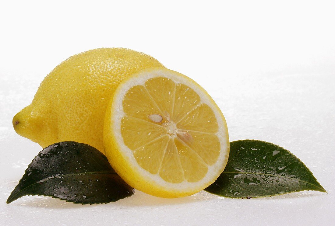 Ganze und halbe Zitrone mit Blättern und Wassertropfen