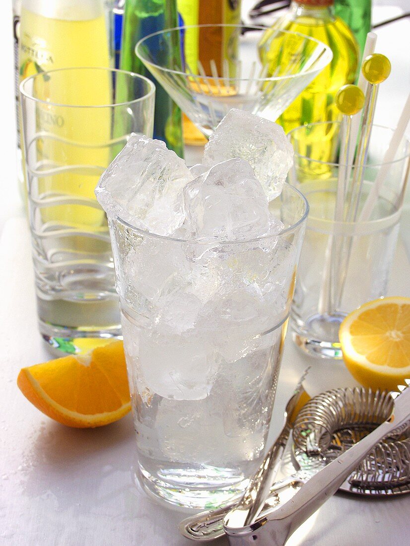 Ice cubes in glass, bar utensils, bottles & citrus fruits
