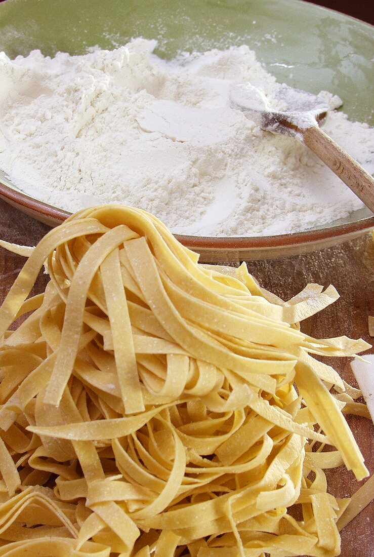 Selbstgemachte Tagliatelle und Mehl auf Holzschneidebrett