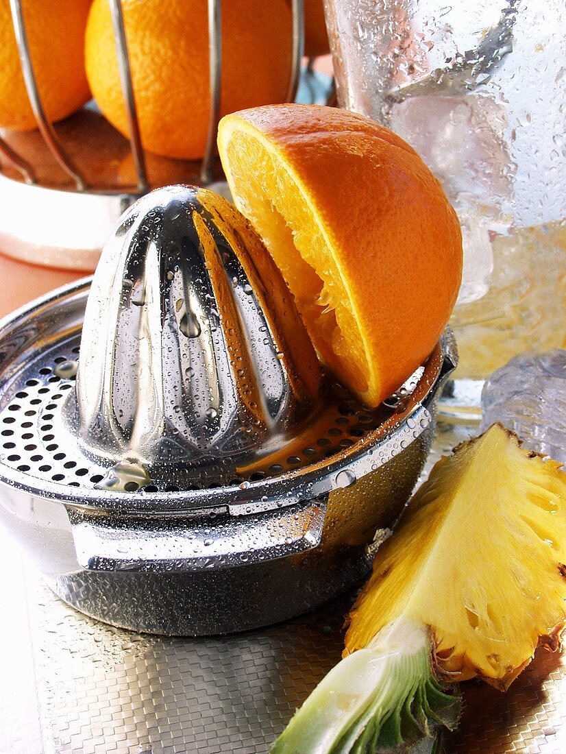 Orange auf Zitruspresse, Ananas und Eiswürfel