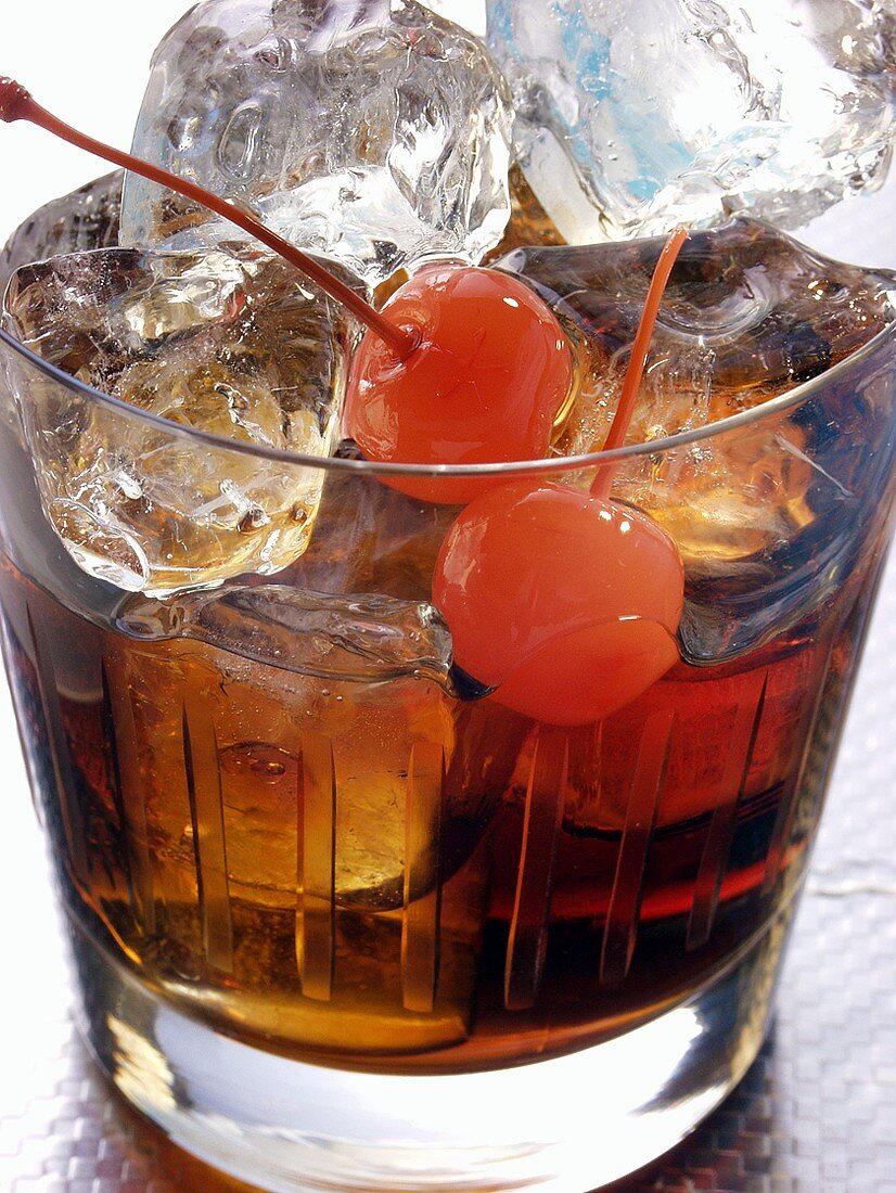 Drink mit Rum, Eiswürfeln und Cocktailkirschen