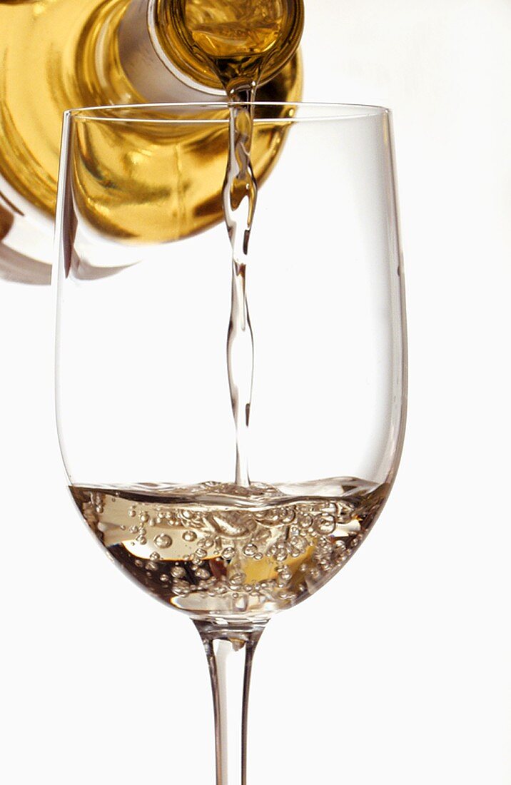 Weißwein aus Flasche in Glas einschenken