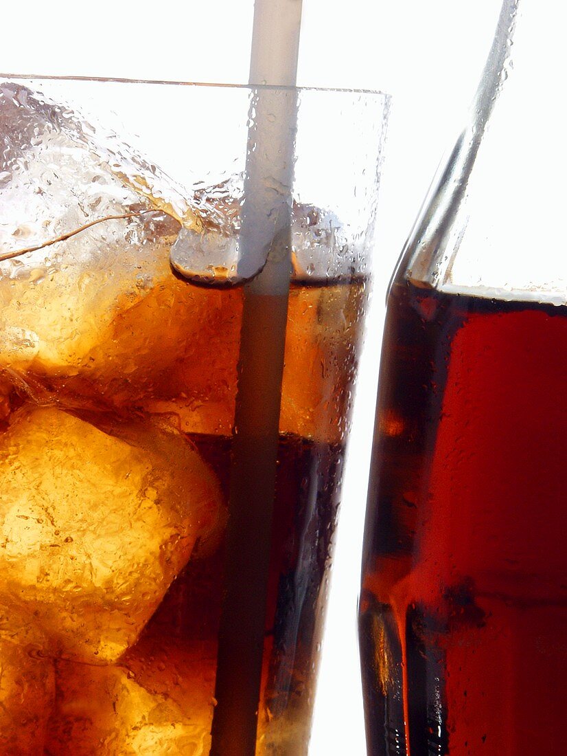 Cola in bottle and glass with ice cubes and straw