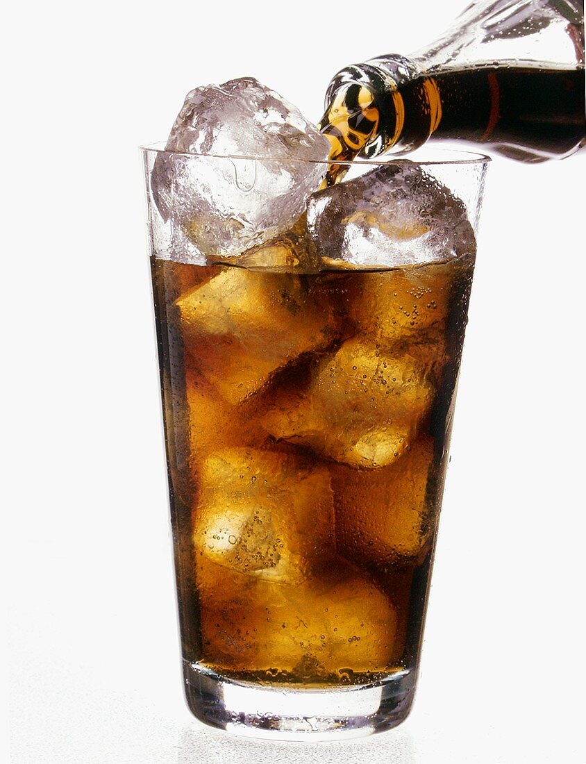 Pouring Cola into glass with ice cubes
