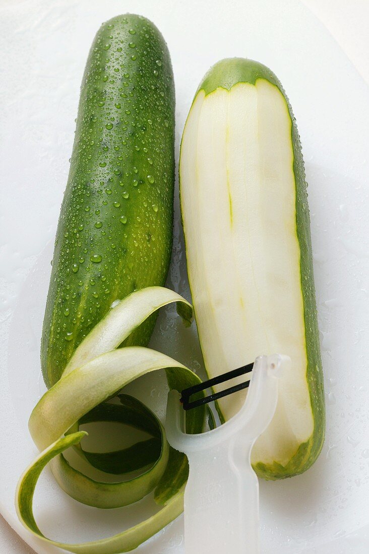 Zwei Salatgurken mit Wassertropfen, eine teilweise geschält