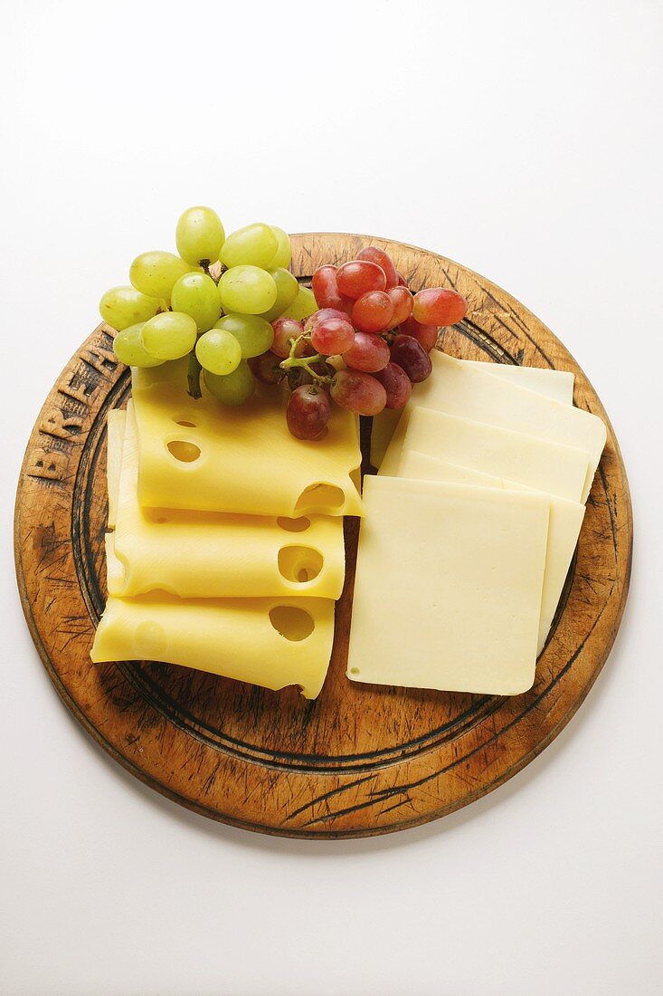 Emmental and American cheese with grapes on wooden plate