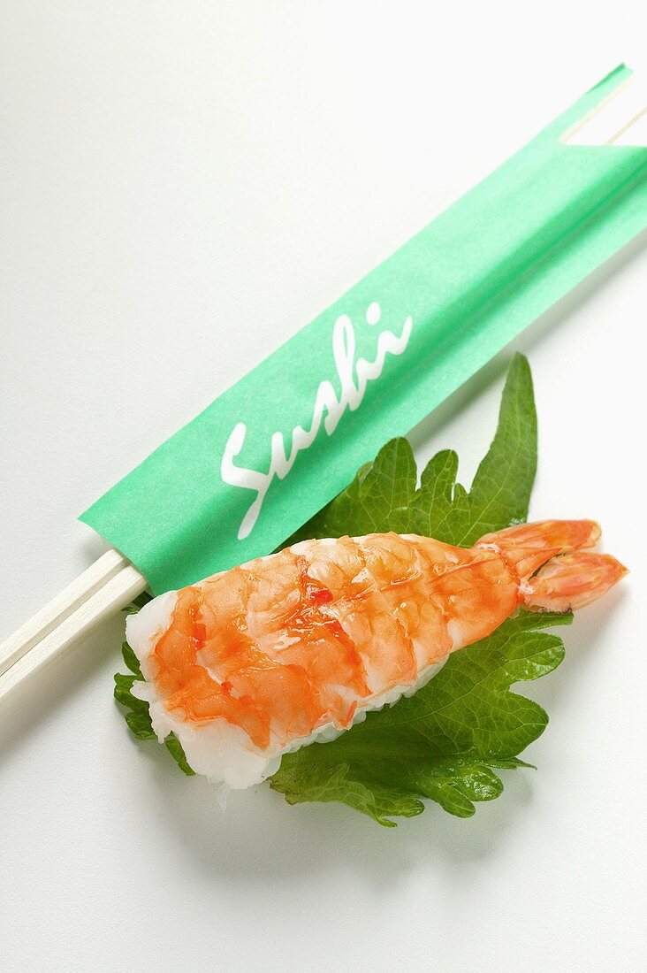 Nigiri sushi with shrimp on shiso leaf; chopsticks