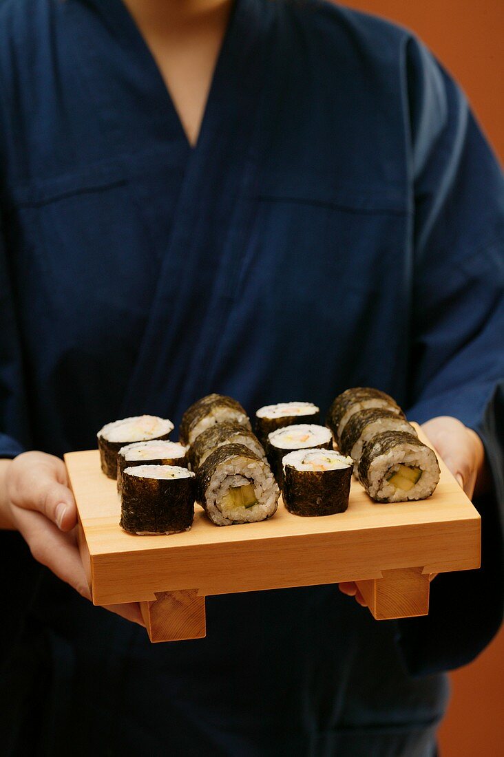 Person im blauen Kimono serviert Maki-Sushi
